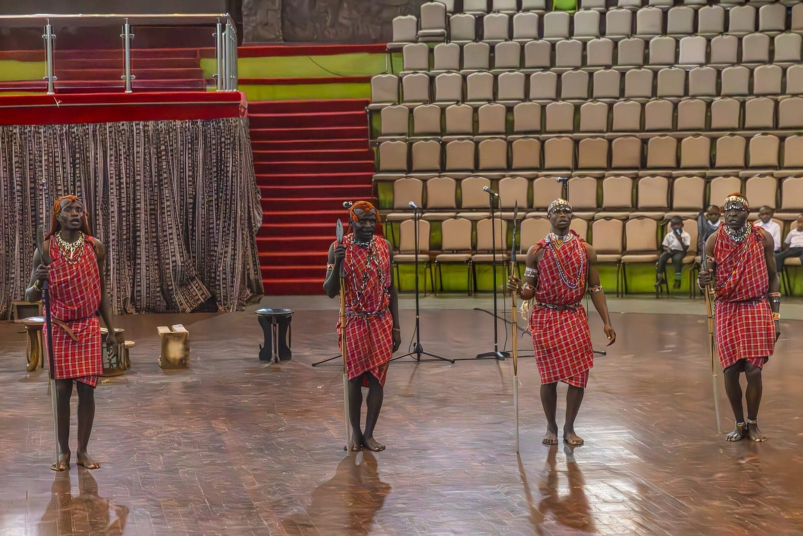 Performers in red shukas on stage in the auditorium at Bomas of Kenya